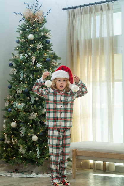 Criança feliz com chapéu de Papai Noel perto da árvore de natal em casa