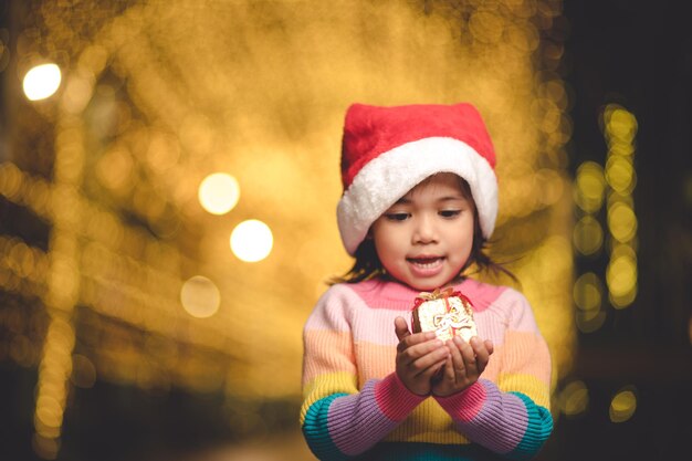 Criança feliz com chapéu de Papai Noel vermelho segurando os presentes de Natal. Época de Natal.