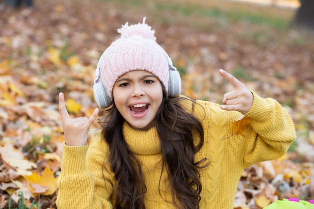 Criança feliz com chapéu se divertindo enquanto ouve música em fones de ouvido ao ar livre no parque, diversão.