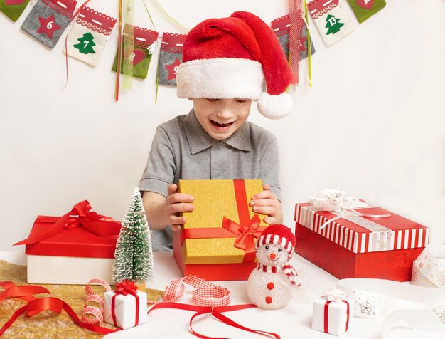 Criança feliz com chapéu vermelho de Papai Noel procurando presente de Natal na caixa Natal e Ano Novo