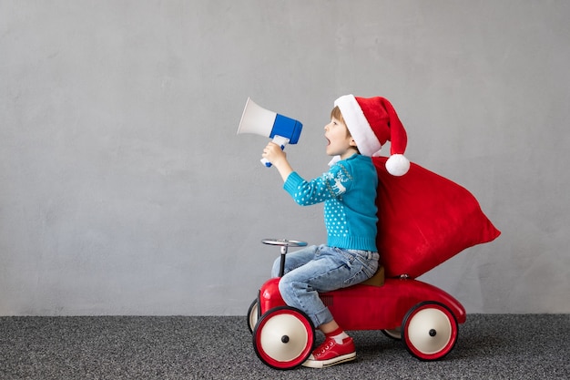 Criança feliz com fantasia de Natal Criança andando no carro de brinquedo Criança engraçada gritando no alto-falante