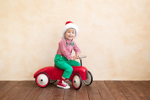 Criança feliz com fantasia de Papai Noel brincando em casa. Garoto engraçado dirigindo o carro de brinquedo. Conceito de férias de natal