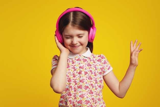 Criança feliz com fones de ouvido rosa, ouvindo música e dançando com os olhos fechados