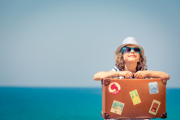 Foto criança feliz com mala na praia criança goza de férias de verão no mar conceito de viagens e férias