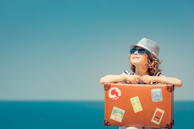 Criança feliz com mala na praia Criança goza de férias de verão no mar Conceito de viagens e férias