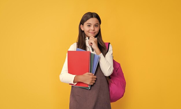 Foto criança feliz com mochila escolar e caderno de trabalho em fundo amarelo