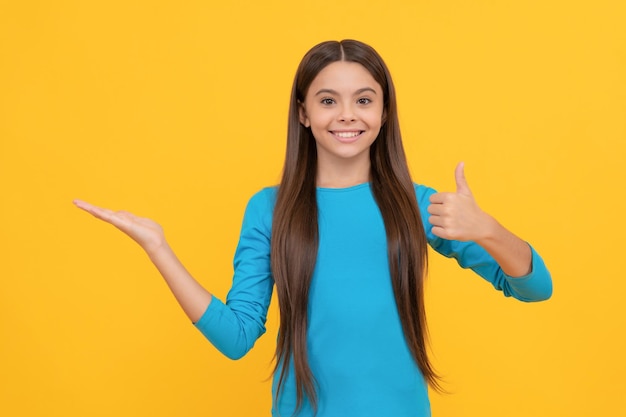 Criança feliz com o polegar para cima apresentando o produto em fundo amarelo com anúncio de espaço de cópia