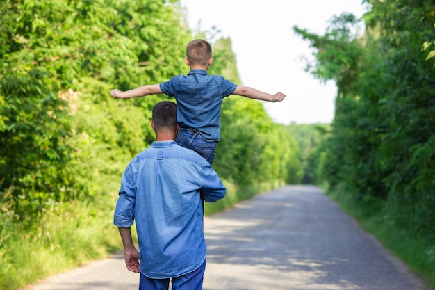 Criança feliz com os pais nos ombros caminha pela estrada no fundo do parque