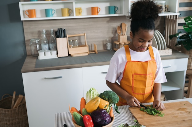 Criança feliz com pele negra com salada de legumes na cozinha