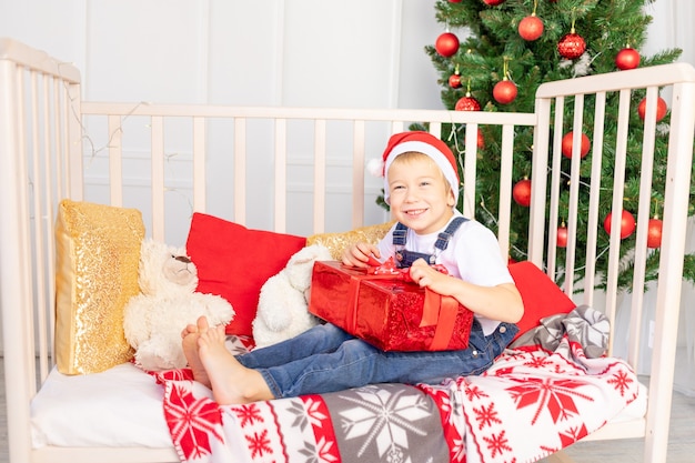 Criança feliz com um chapéu vermelho segurando um presente perto da árvore de Natal