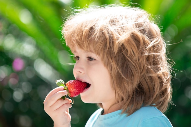 Criança feliz come morangos no fundo verde da primavera
