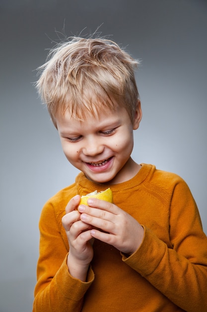 Criança feliz comendo limão no estúdio cinza