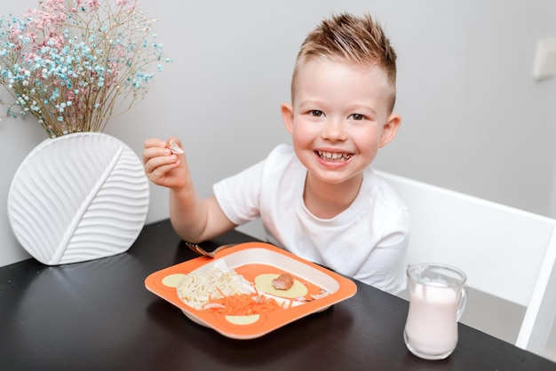 Criança feliz comendo macarrão delicioso na mesa da cozinha