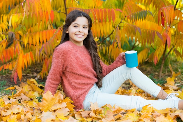 Criança feliz da menina com a caneca no outono parque colorido fundo de folhagem. ideias aconchegantes para um piquenique de outono. bebida quente. cuidados de saúde. criança gosta de bebida quente de outono. criança relaxe na árvore de outono.