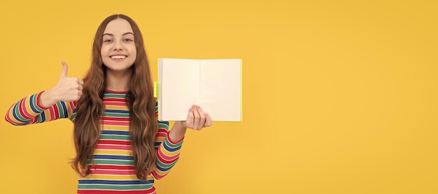 Criança feliz dá polegares para cima gesto com a mão segurando o livro aberto para o espaço de cópia fundo amarelo satisfeito Cartaz isolado horizontal da aluna da escola Retrato de cabeçalho do banner do espaço de cópia da estudante