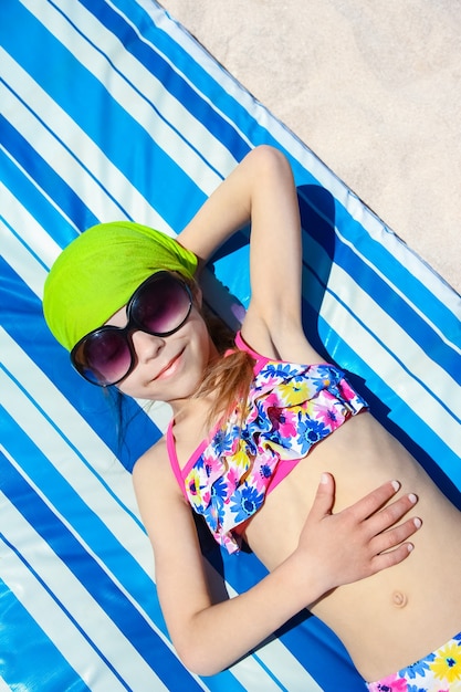 Criança feliz de óculos tomando sol no fundo da praia