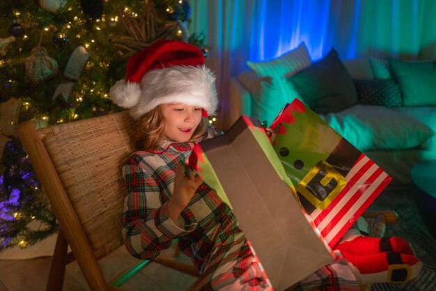 Criança feliz de pijama perto da árvore de natal em casa com a tradicional árvore de natal