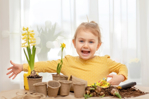 Criança feliz e emocional cuidando de flores da primavera com ferramentas, luvas de jardinagem, terra para vasos