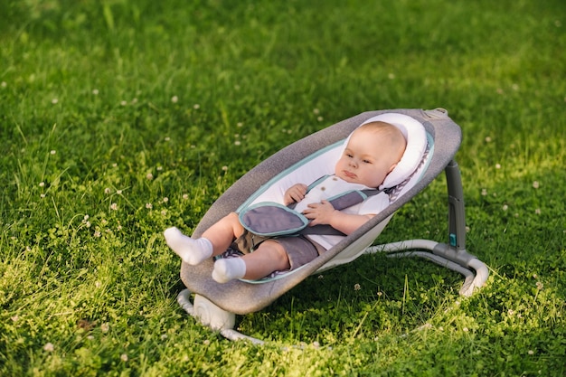 Criança feliz e fofa sentada em uma cadeira na grama ao ar livre no verão