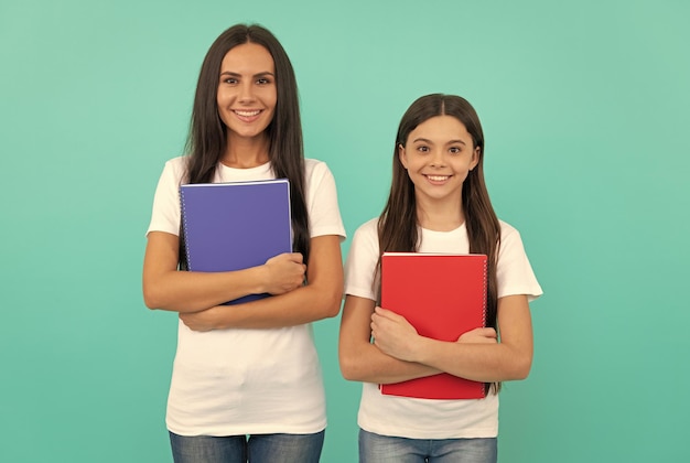 Criança feliz e mãe ou professor seguram o livro de exercícios da escola para estudar educação