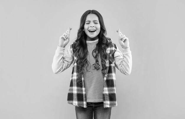 Criança feliz em camisa quadriculada cruzou os dedos fazendo desejo na moda de fundo rosa