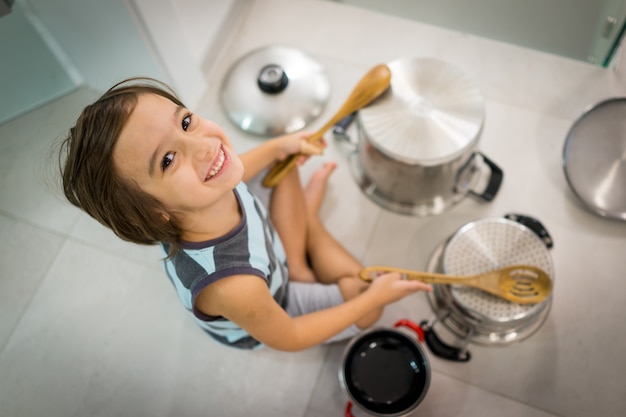 Criança feliz em casa brincando com pratos como instrumentos musicais e bateria