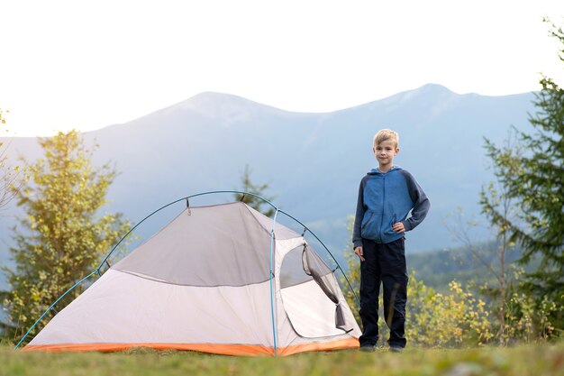 Criança feliz em pé perto de uma barraca de turista em um acampamento na montanha