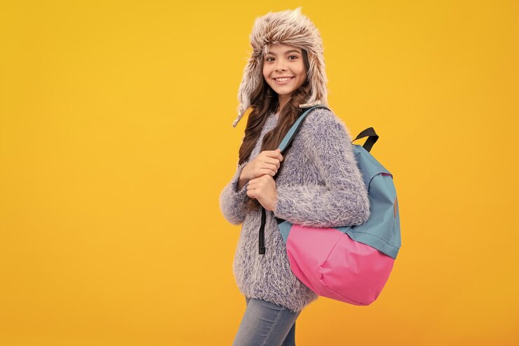 Foto criança feliz em suéter e chapéu de fone de ouvido com mochila em fundo amarelo com escola de espaço de cópia