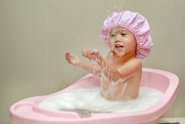 Criança feliz em um boné de espuma na banheira