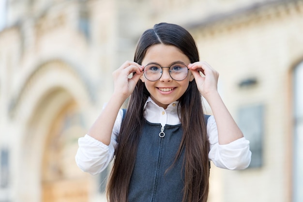 Criança feliz em uniforme escolar colocar óculos de moda para ver bem a visão ao ar livre