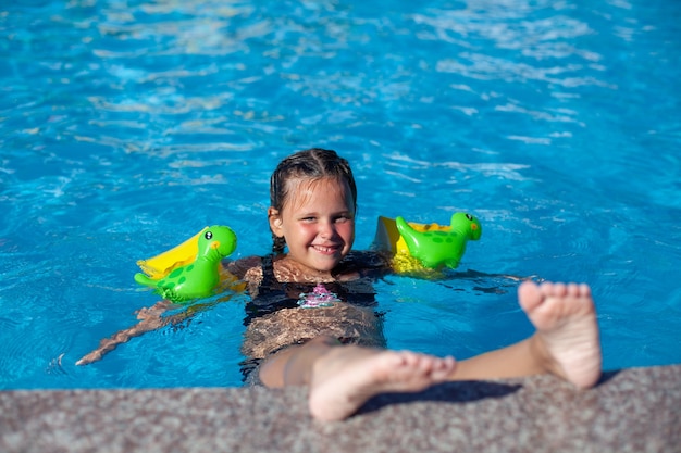 Criança feliz está curtindo as férias de verão, garotinha encantadora em braçadeiras infláveis para nadar sagacidade ...