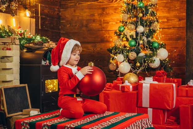 Criança feliz está vestindo roupas de Papai Noel, decorando a árvore de Natal segurar bugiganga conceito de Natal ...