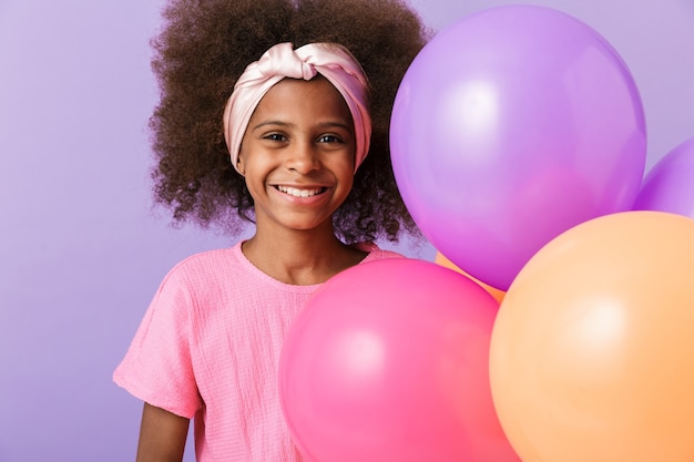 criança feliz linda garota africana posando com balões isolados sobre a parede roxa.