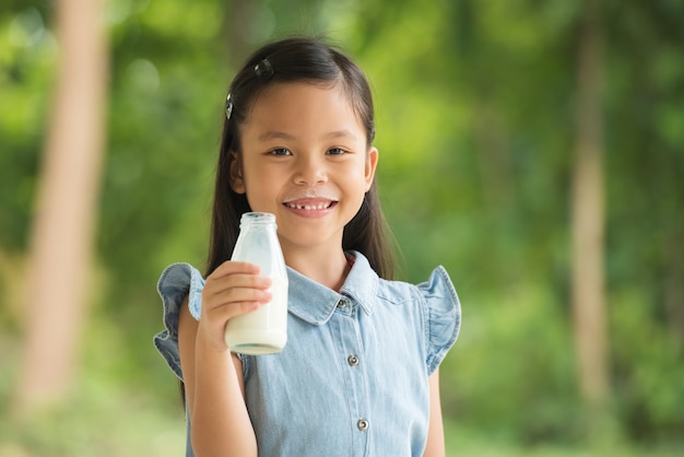 Criança feliz, menina asiática, desfrutando de pequeno-almoço saudável e bebendo leite