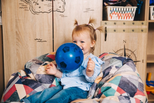 Criança feliz, menina brincando com uma bola enquanto está sentado em uma cadeira macia. criança brinca com uma bola.