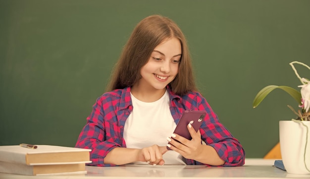 Criança feliz na escola conversando no telefone na comunicação de fundo do quadro-negro