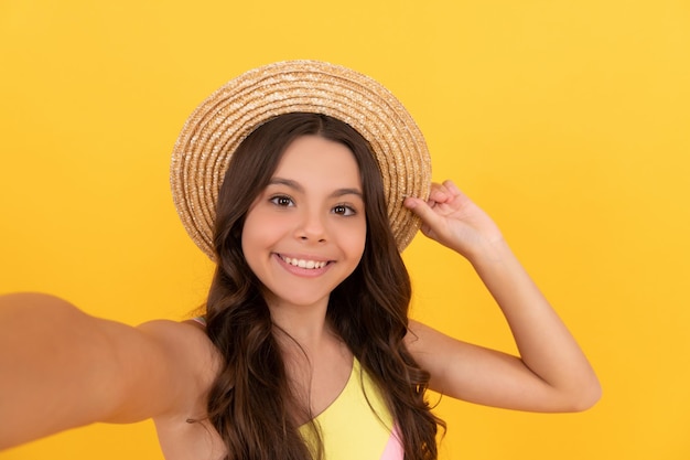 Criança feliz no chapéu de palha de verão fazendo selfie em fundo amarelo se divertindo