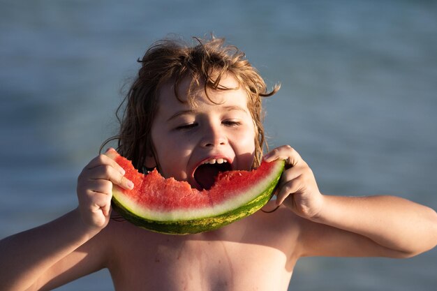 Criança feliz no mar com melancia criança engraçada come melancia criança relaxando na praia do mar de verão k