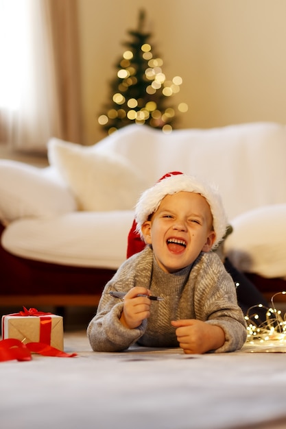 Criança feliz no natal escreva uma carta para o papai noel no chapéu de natal escrevendo a lista de desejos do presente próximo ao natal