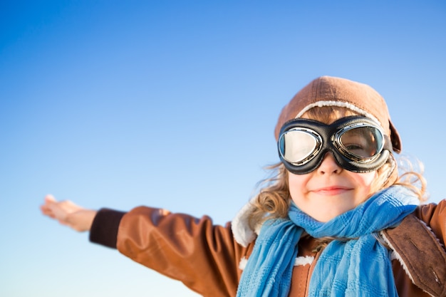 Criança feliz no papel de piloto contra o fundo do céu azul de inverno