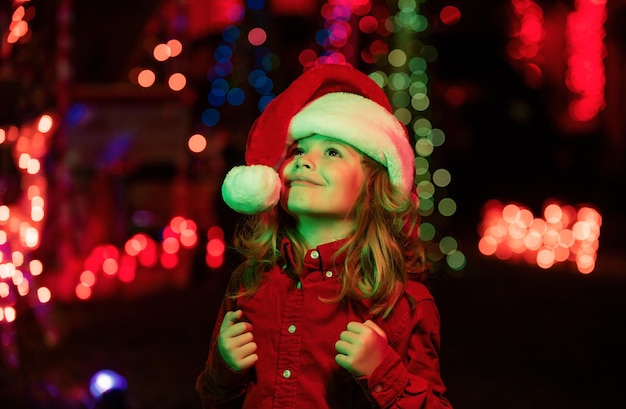 Criança feliz olha para o céu na noite de Natal criança no quintal da casa de noite decorada