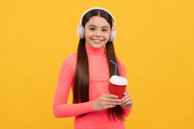 Criança feliz ouve música em fones de ouvido com copo de papel no estilo de vida de fundo amarelo