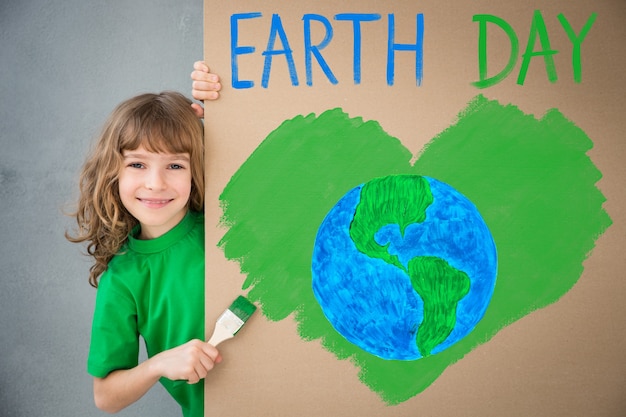 Criança feliz pintando o papelão com a cor verde. garoto se divertindo em casa. conceito de férias do dia da terra na primavera