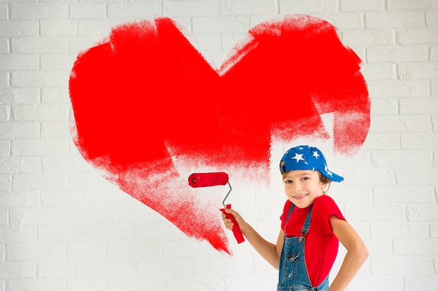 Criança feliz pintando um grande coração vermelho na parede. Garota engraçada brincando em casa. Cartão de dia dos namorados. Renovação e conceito de design