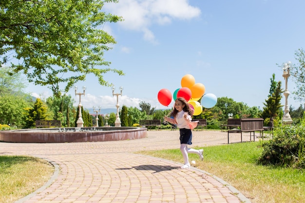 Criança feliz pulando com balões de brinquedo colorido ao ar livre criança sorridente se divertindo no campo verde primavera