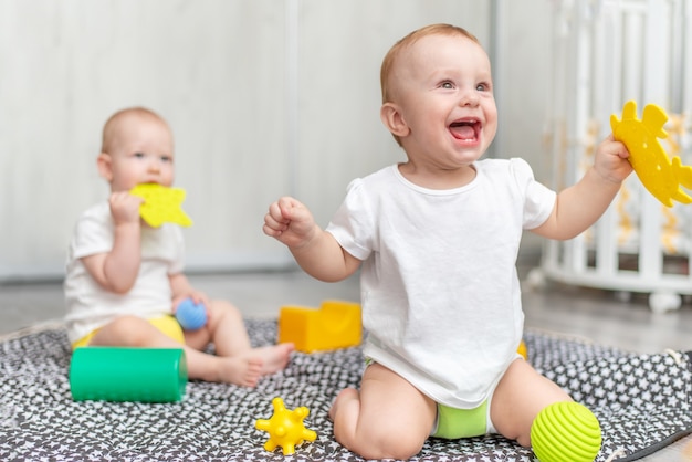 Criança feliz ri e brinca com o amigo nos brinquedos da sala enquanto está sentada no chão