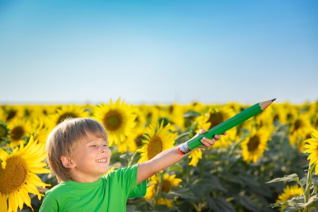 Criança feliz se divertindo no campo de primavera de girassóis Retrato ao ar livre da criança contra o fundo do céu azul
