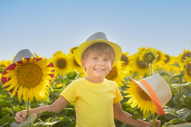 Criança feliz se divertindo no campo primavera de girassóis. Retrato ao ar livre da criança contra o fundo do céu azul