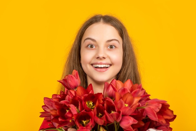 Criança feliz segura flores de tulipa da primavera em fundo amarelo