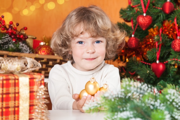 Criança feliz segurando bolas de ouro em um fundo de Natal decorado